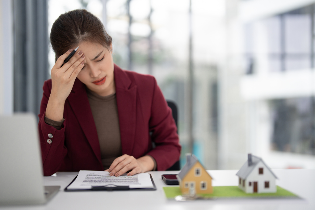Woman upset on computer with small house figurines on her desk.